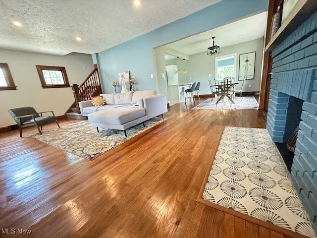 Living area with a textured ceiling, a brick fireplace, wood finished floors, stairway, and recessed lighting