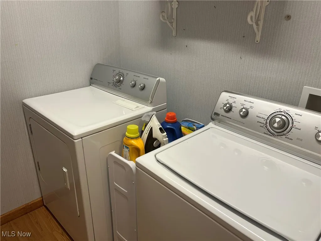 Laundry area with wallpapered walls, wood finished floors, and washing machine and dryer