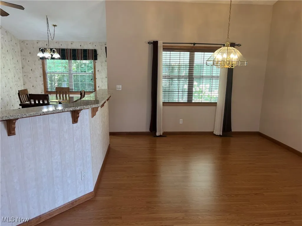 Kitchen with a chandelier, hanging light fixtures, dark wood-type flooring, a kitchen bar, and dark stone countertops