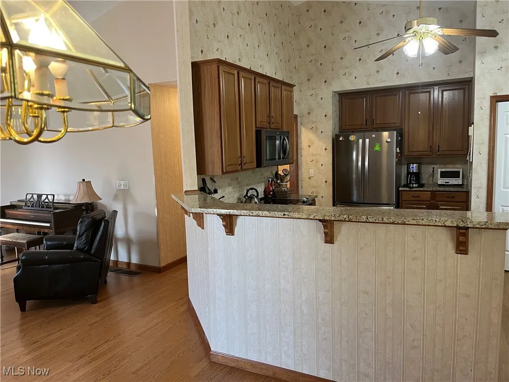 Kitchen with a peninsula, a breakfast bar, stainless steel appliances, light wood finished floors, and a chandelier