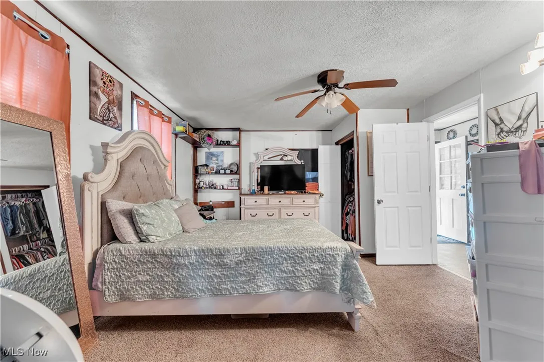 Bedroom featuring a textured ceiling, light colored carpet, and ceiling fan