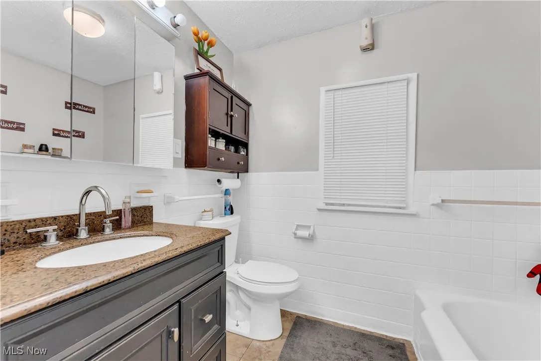 Bathroom with a garden tub, vanity, a textured ceiling, tile walls, and wainscoting