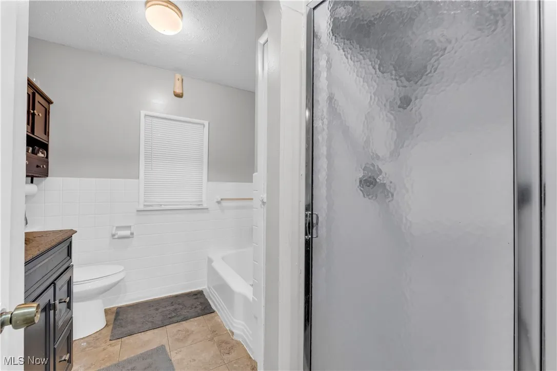 Bathroom with vanity, a stall shower, tile walls, a wainscoted wall, and a textured ceiling