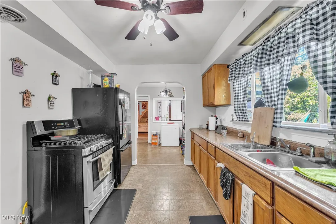 Kitchen with stainless steel gas range, arched walkways, brown cabinets, light countertops, and freestanding refrigerator