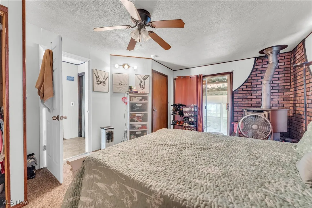 Bedroom featuring light carpet, a wood stove, ceiling fan, a textured ceiling, and access to outside