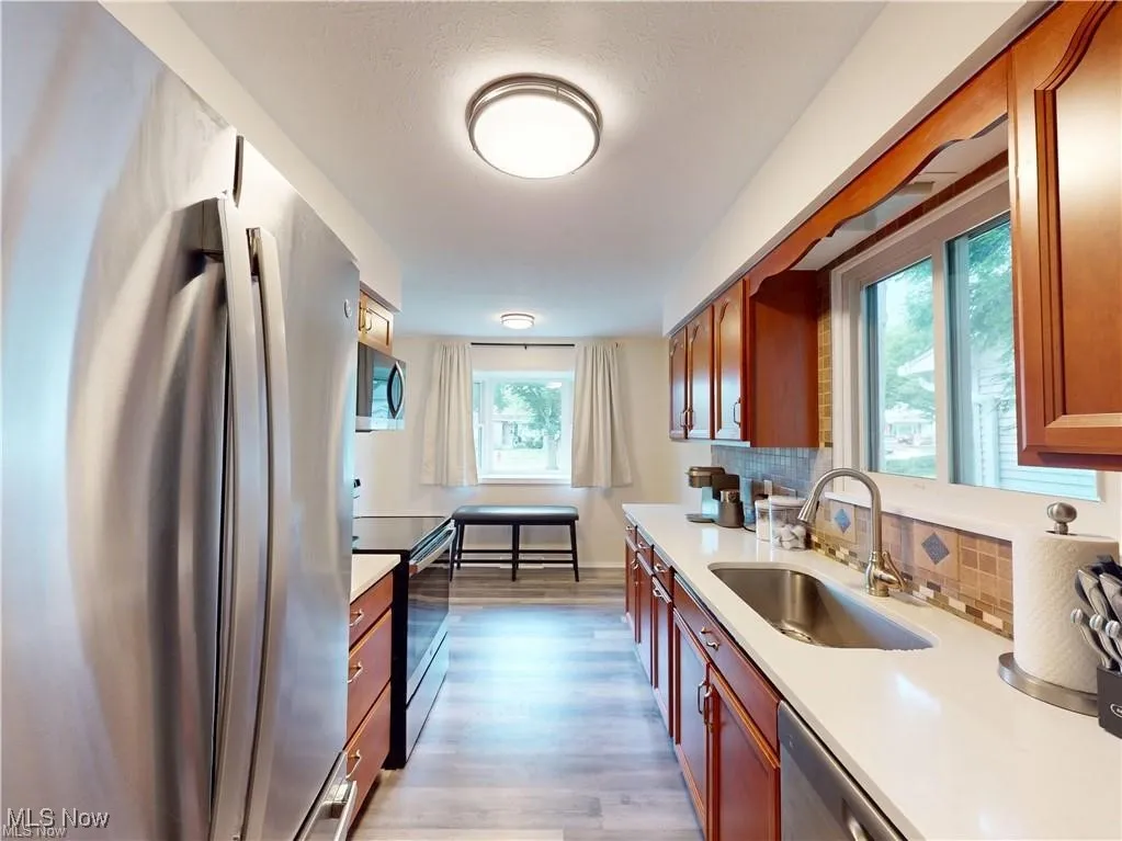 Kitchen featuring appliances with stainless steel finishes, light wood finished floors, decorative backsplash, light stone counters, and dark brown cabinets
