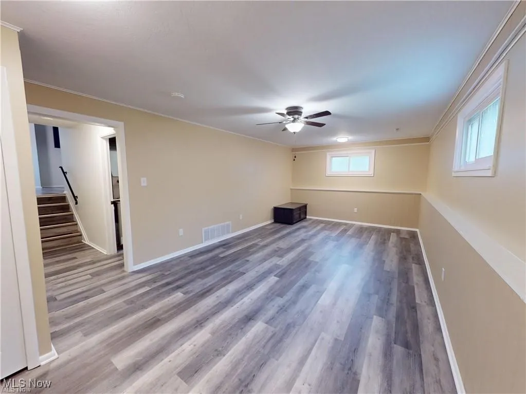 Unfurnished living room with light wood-style flooring, crown molding, ceiling fan, and stairway