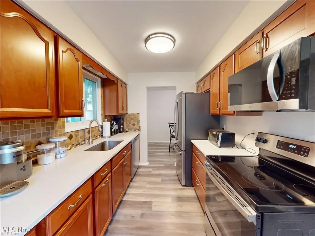 Kitchen featuring stainless steel appliances, brown cabinetry, backsplash, light wood-style floors, and light stone counters