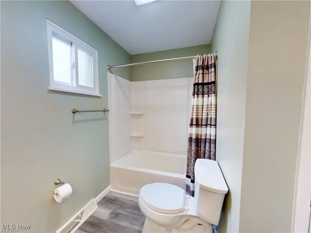 Full bath featuring wood finished floors and shower / bath combination with curtain