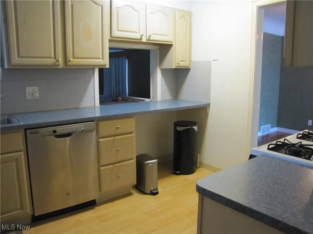 Kitchen with decorative backsplash, dishwasher, light wood finished floors, and dark countertops