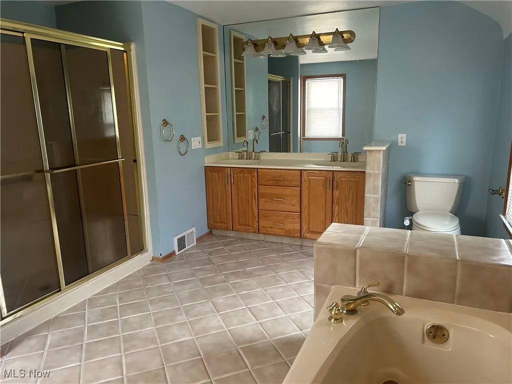 Full bathroom featuring double vanity, light tile patterned floors, a shower stall, and a tub with jets