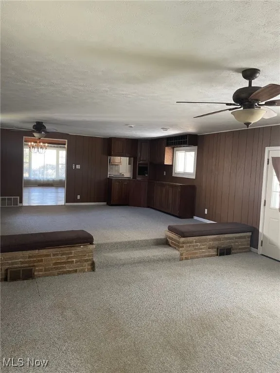 Living area with a ceiling fan, light carpet, a textured ceiling, and wooden walls