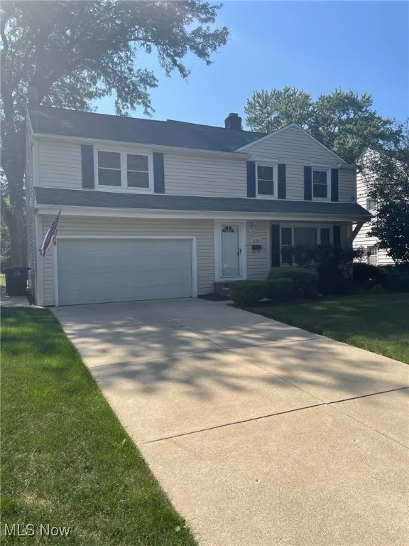 Traditional-style house featuring an attached garage, a chimney, driveway, and a front lawn