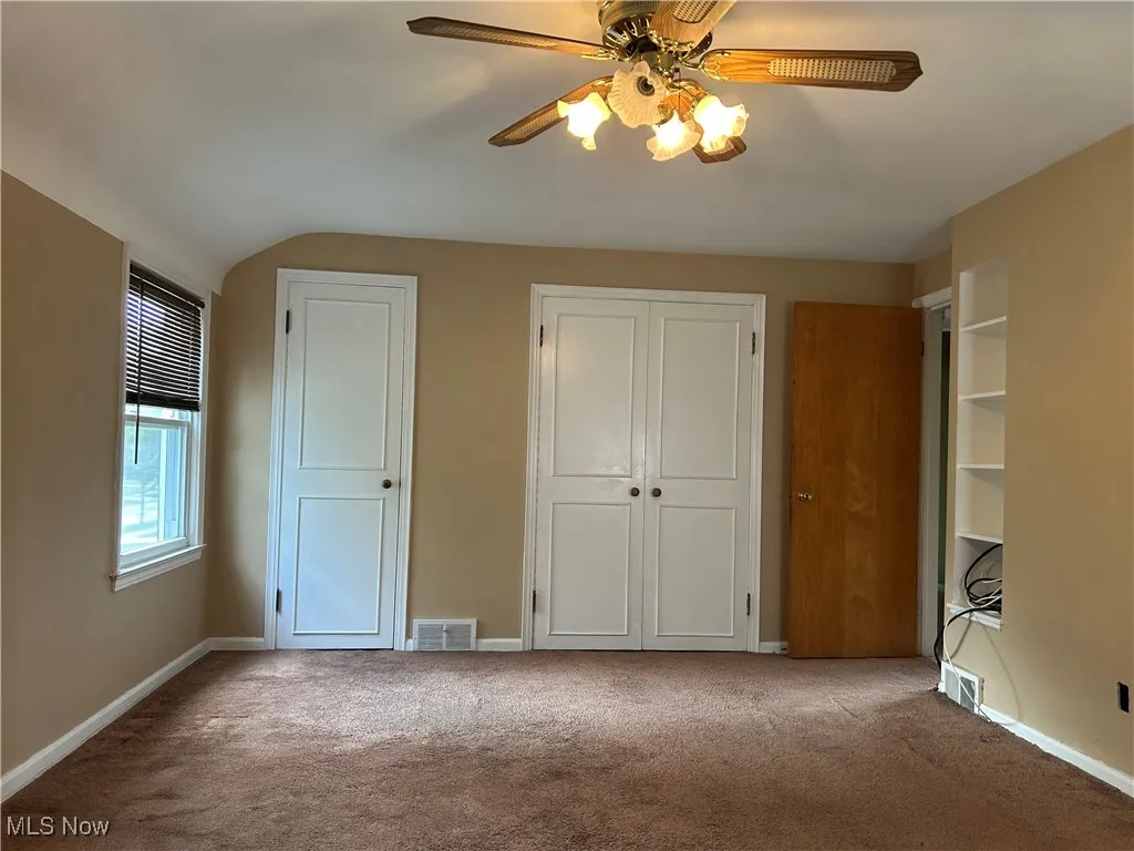 Unfurnished bedroom with carpet flooring, a ceiling fan, and multiple closets