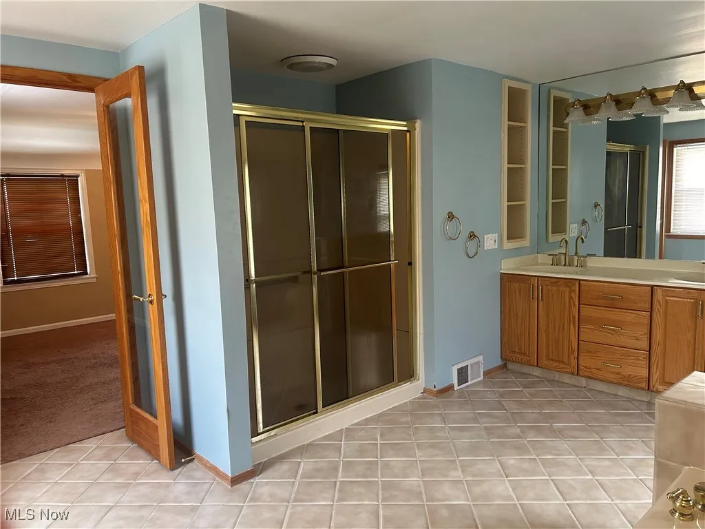 Bathroom with light tile patterned flooring, double vanity, and a shower stall