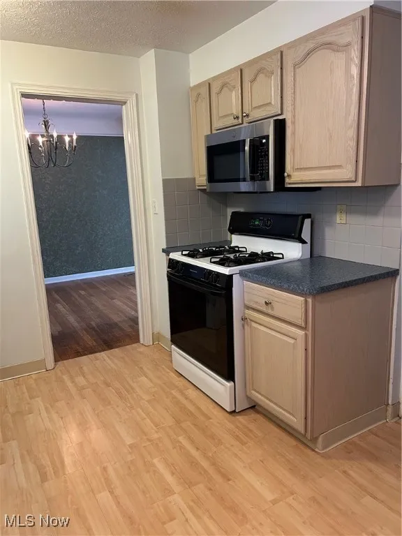 Kitchen featuring white range with gas stovetop, a chandelier, light wood-style flooring, light brown cabinets, and dark countertops