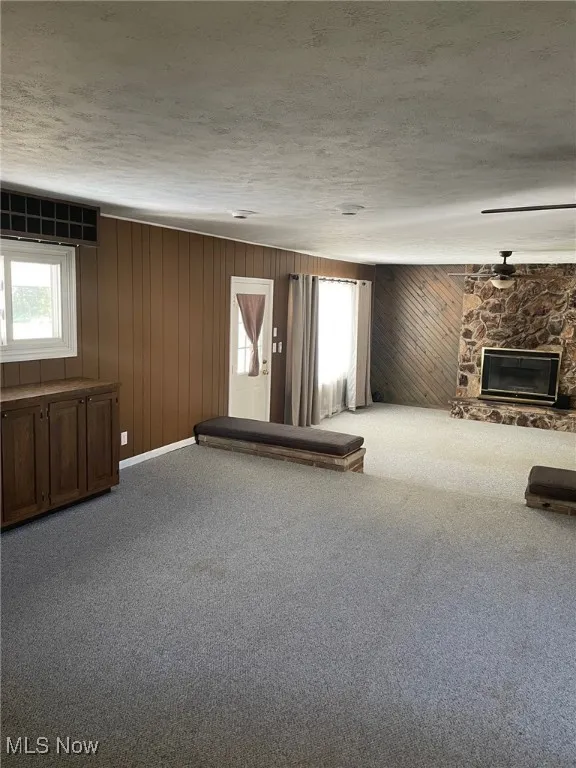Carpeted spare room featuring a textured ceiling, a stone fireplace, and wooden walls