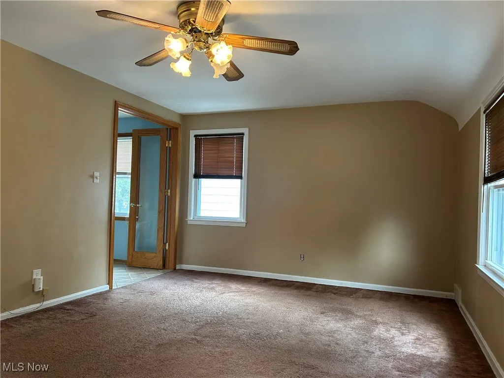Empty room with light colored carpet, vaulted ceiling, and a ceiling fan