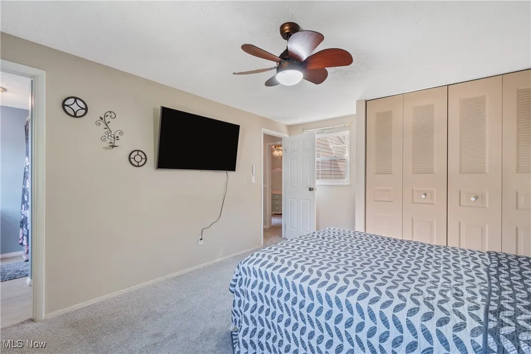 Carpeted bedroom featuring a closet, a ceiling fan, and ensuite bath