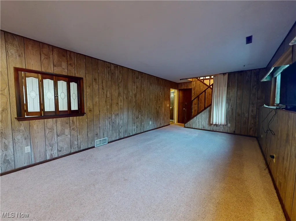 Unfurnished living room featuring wooden walls and stairway
