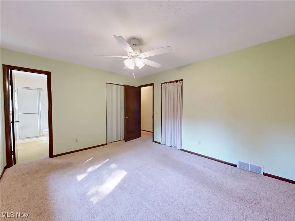 Unfurnished bedroom with light colored carpet, ensuite bath, a ceiling fan, and a closet