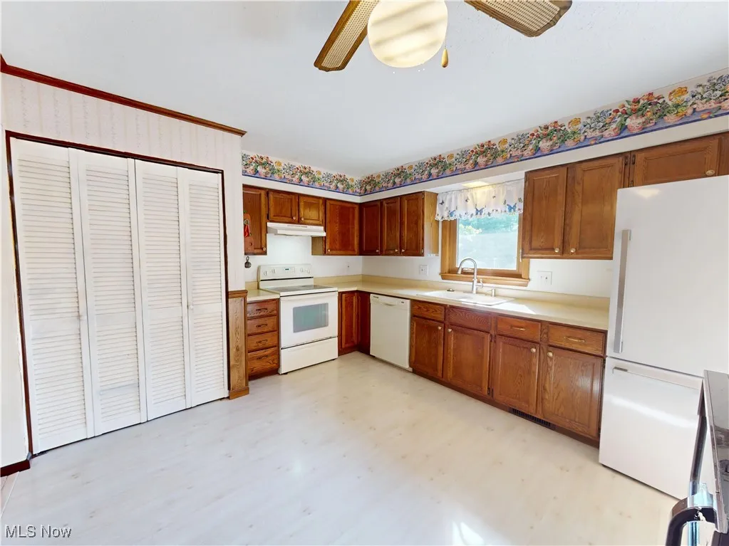 Kitchen with white appliances, light countertops, brown cabinets, a ceiling fan, and under cabinet range hood