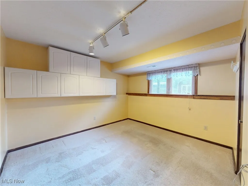 Below grade area featuring rail lighting and light colored carpet