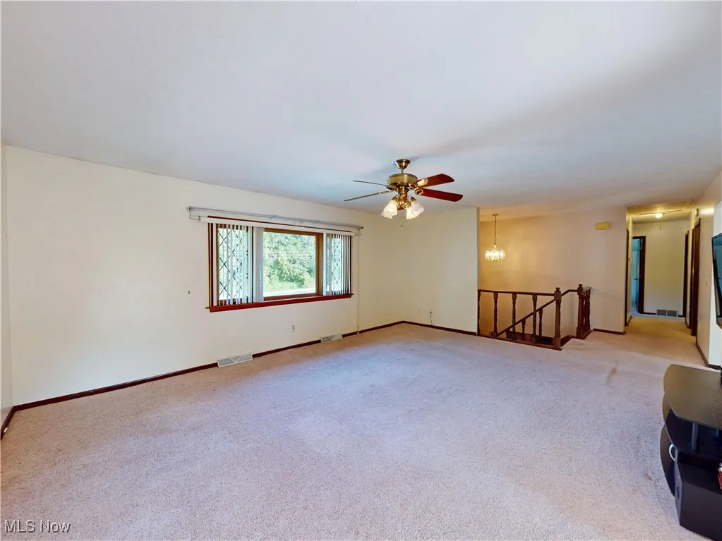 Unfurnished room featuring a chandelier, light colored carpet, and ceiling fan