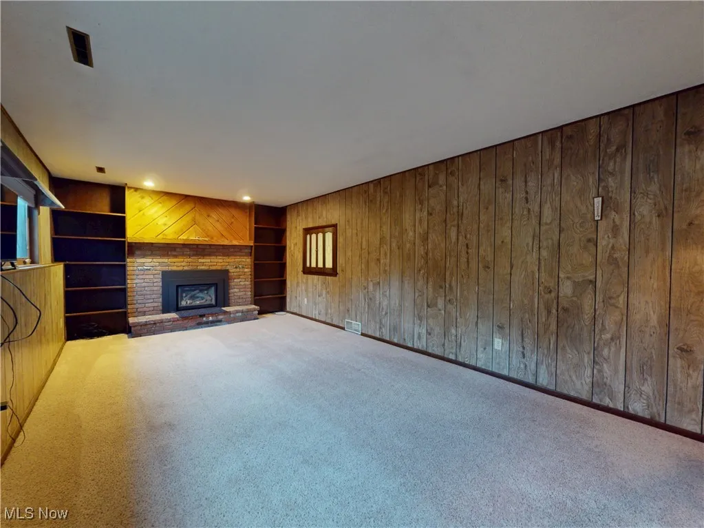 Unfurnished living room featuring carpet, a brick fireplace, wooden walls, and built in features