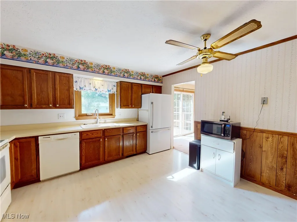 Kitchen featuring white appliances, light countertops, brown cabinets, wallpapered walls, and wooden walls