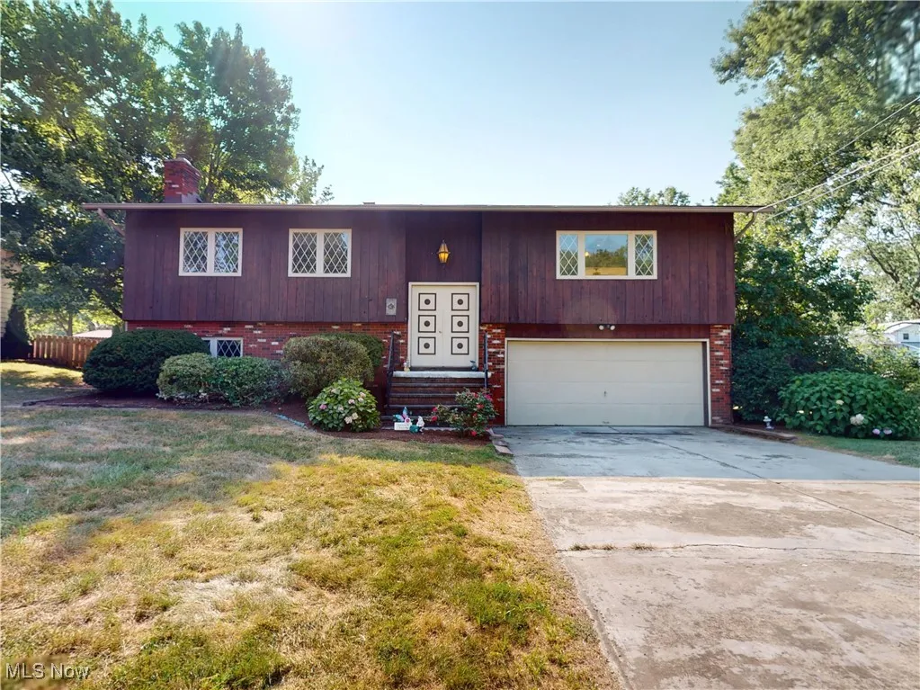 Split foyer home with brick siding, a garage, driveway, a chimney, and a front yard