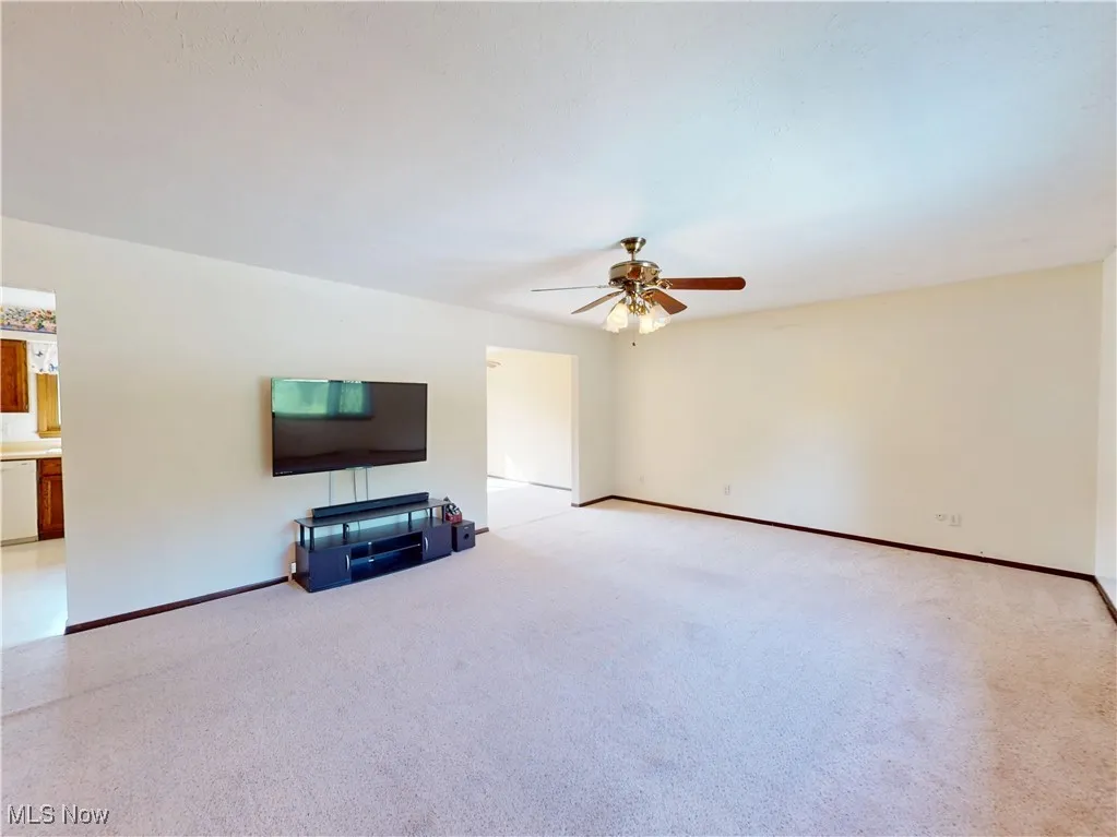 Unfurnished living room featuring light colored carpet and a ceiling fan