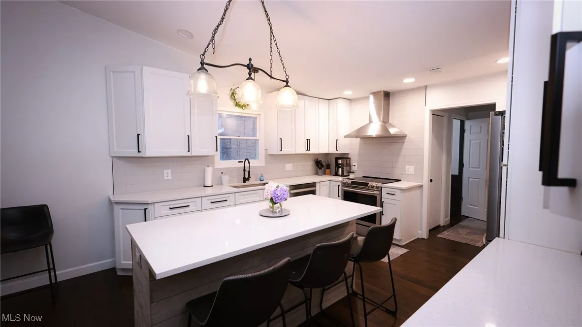 Kitchen featuring white cabinetry, wall chimney range hood, dark wood-type flooring, a kitchen breakfast bar, and recessed lighting