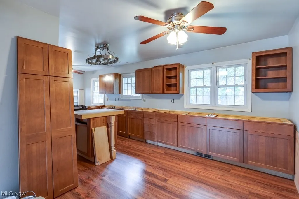 Kitchen with open shelves, brown cabinetry, dark wood-style flooring, a ceiling fan, and a center island