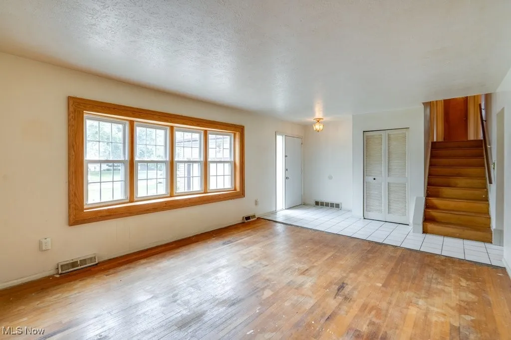 Unfurnished living room with a textured ceiling, hardwood floors, bay windows and stairway