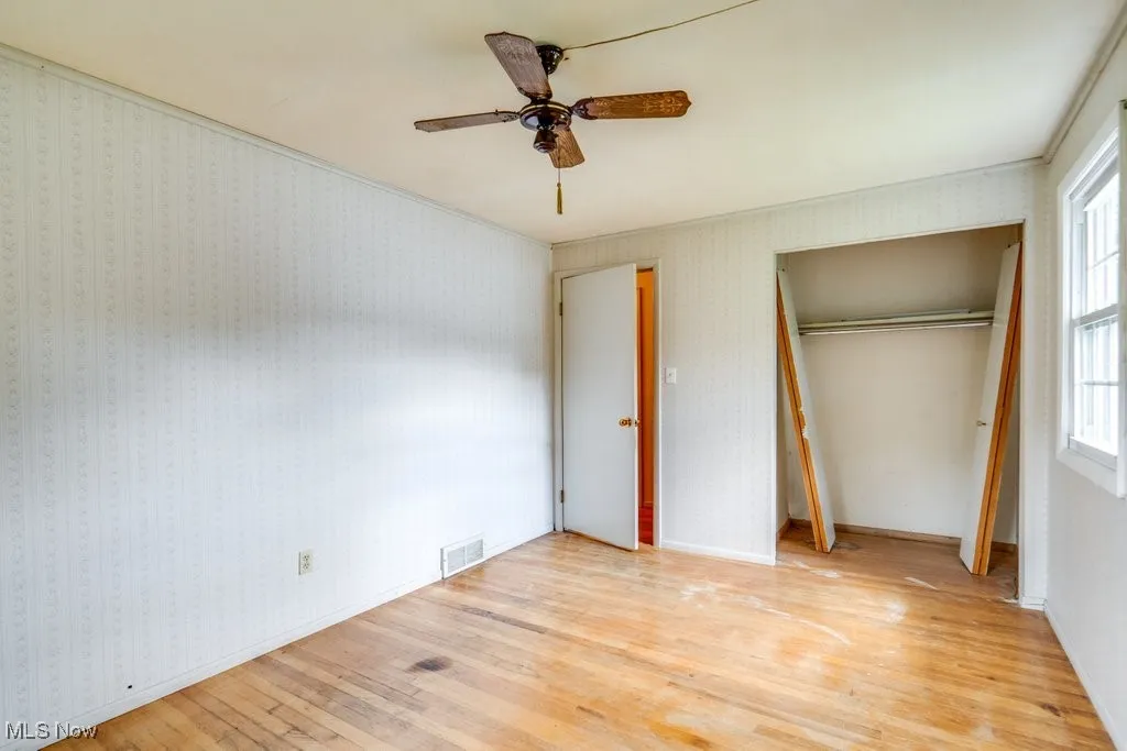 Unfurnished bedroom featuring hardwood / wood-style flooring, ceiling fan, a closet, and wallpapered walls