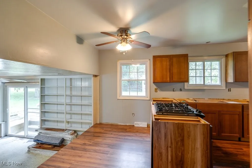 Kitchen featuring brown cabinets, a ceiling fan, dark wood finished floors, and stainless steel gas cooktop