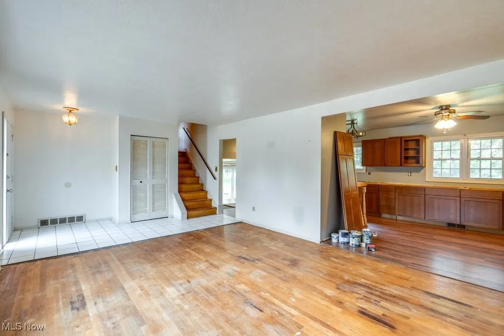 Unfurnished living room featuring light wood-type flooring, plenty of natural light, a ceiling fan, and stairway