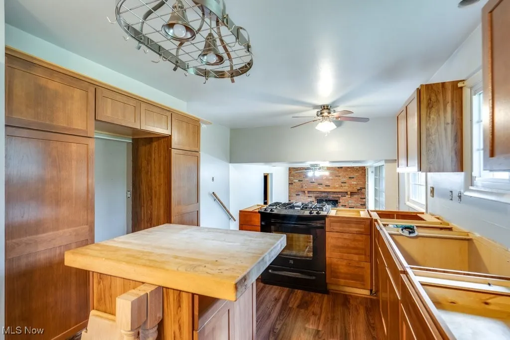 Kitchen with black gas stove, ceiling fan, dark wood finished floors, brown cabinetry, and butcher block countertops