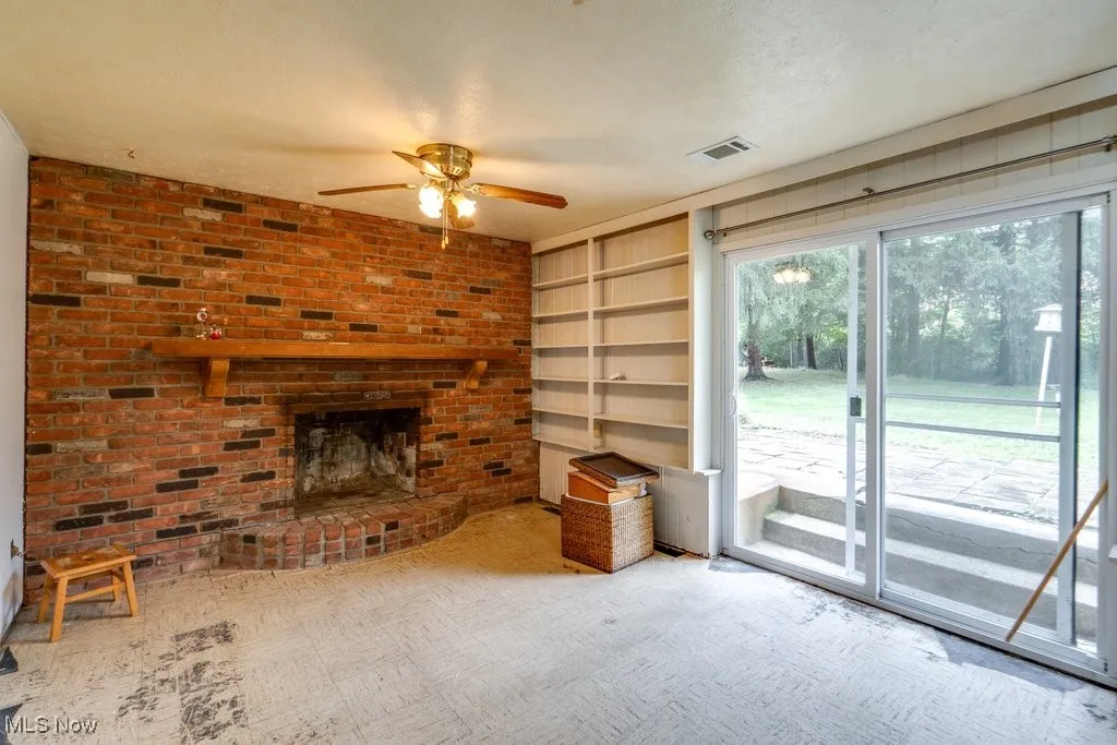 Unfurnished living room featuring a ceiling fan, a brick fireplace, built in shelves, brick wall, and a textured ceiling
