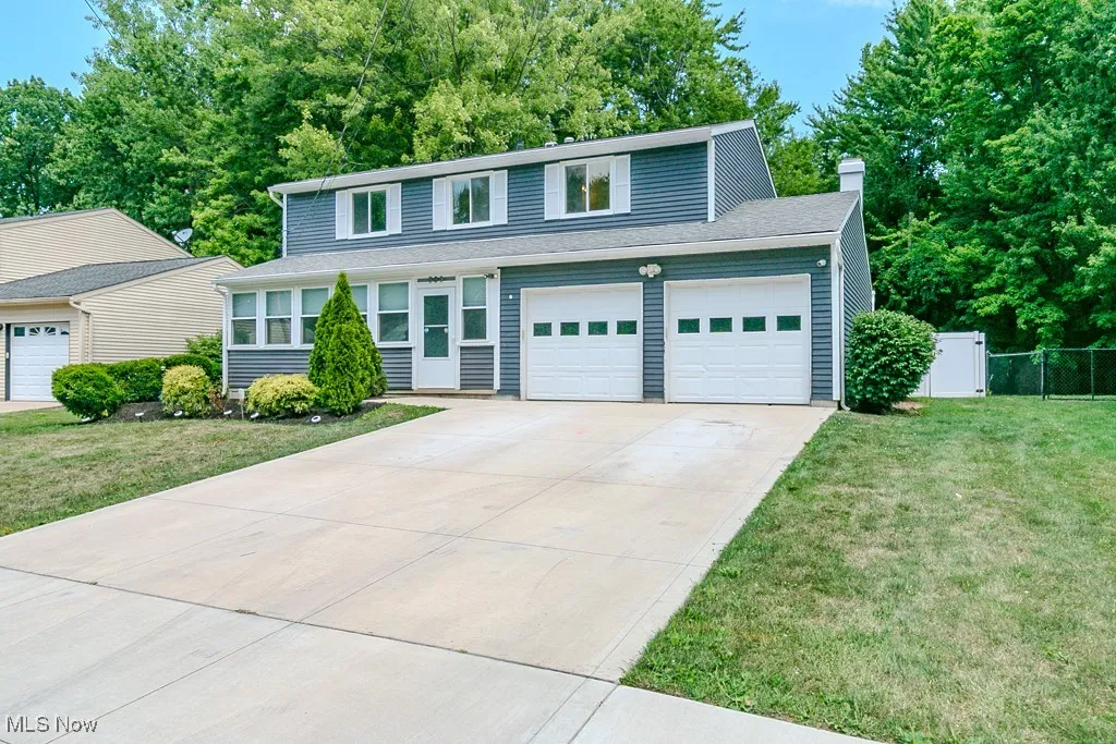 Traditional-style house featuring driveway, a chimney, view of scattered trees, a garage, and a shingled roof