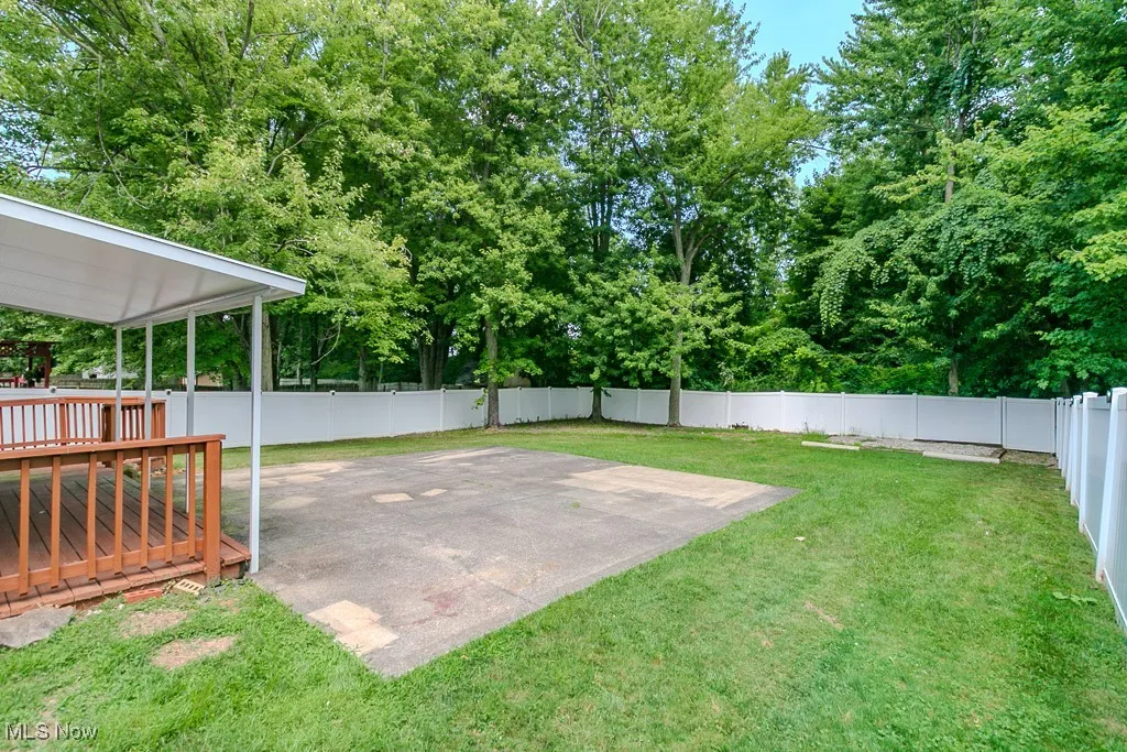 Fenced backyard featuring a patio area, a deck, and view of scattered trees