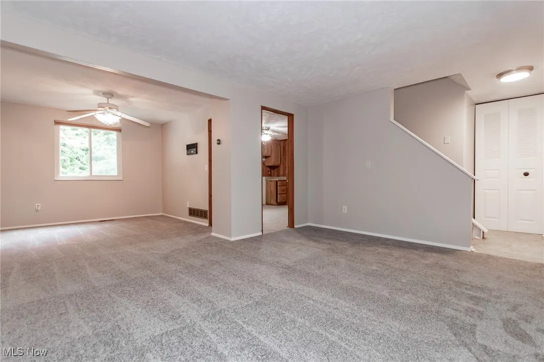 Unfurnished living room featuring light carpet, entry way, dining room and doorway to the kitchen.