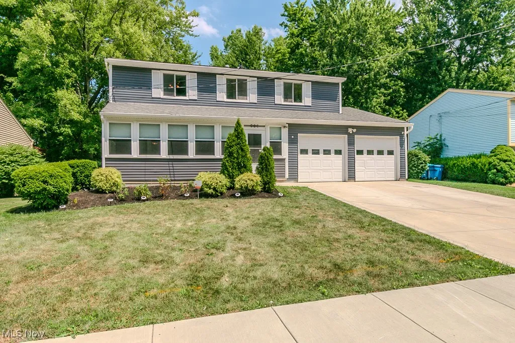 Traditional-style house featuring driveway, a front lawn, view of wooded area, and an attached garage