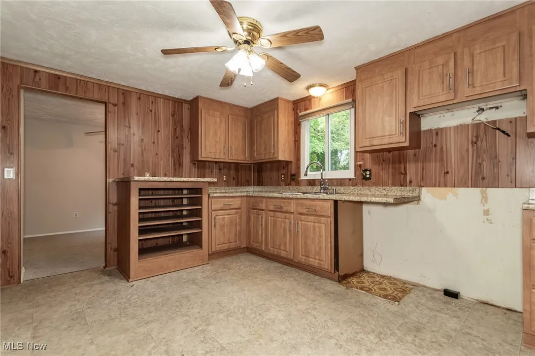 Kitchen featuring wood walls, brown cabinets, ceiling fan, and light countertops