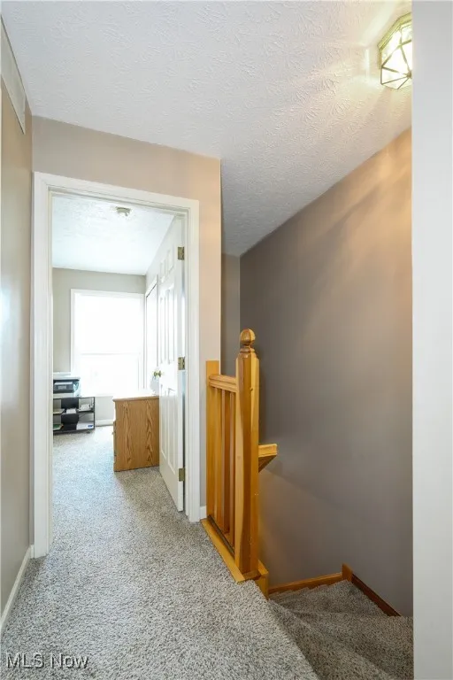 Hallway with an upstairs landing, light carpet, and a textured ceiling