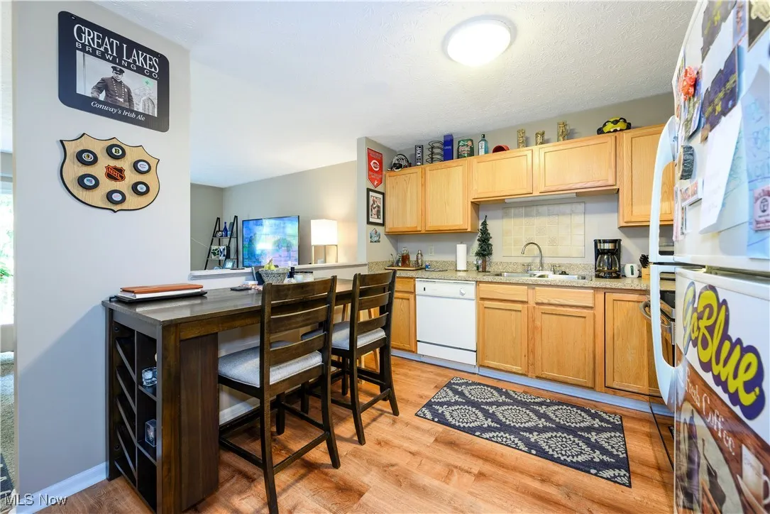 Kitchen with white appliances, light wood-style floors, decorative backsplash, light stone countertops, and light brown cabinets