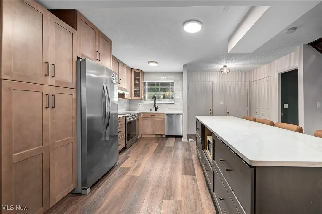 Kitchen with glass insert cabinets, appliances with stainless steel finishes, a kitchen breakfast bar, light stone countertops, and dark wood-style flooring