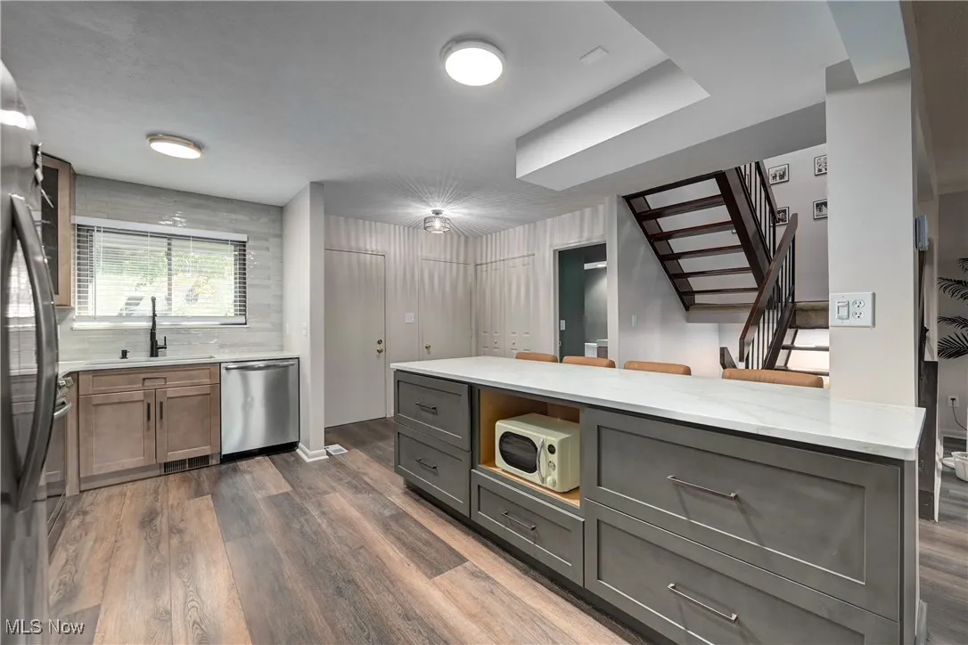 Kitchen with dark wood-style flooring, light stone counters, stainless steel dishwasher, and white microwave