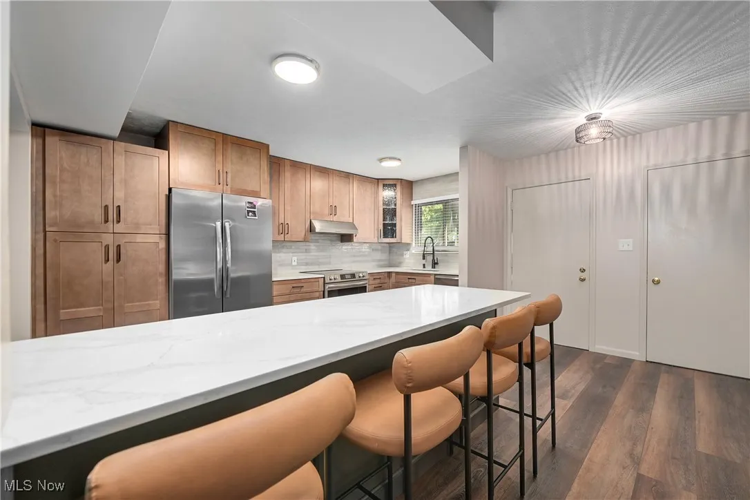Kitchen with a breakfast bar area, light stone countertops, decorative backsplash, and stainless steel appliances